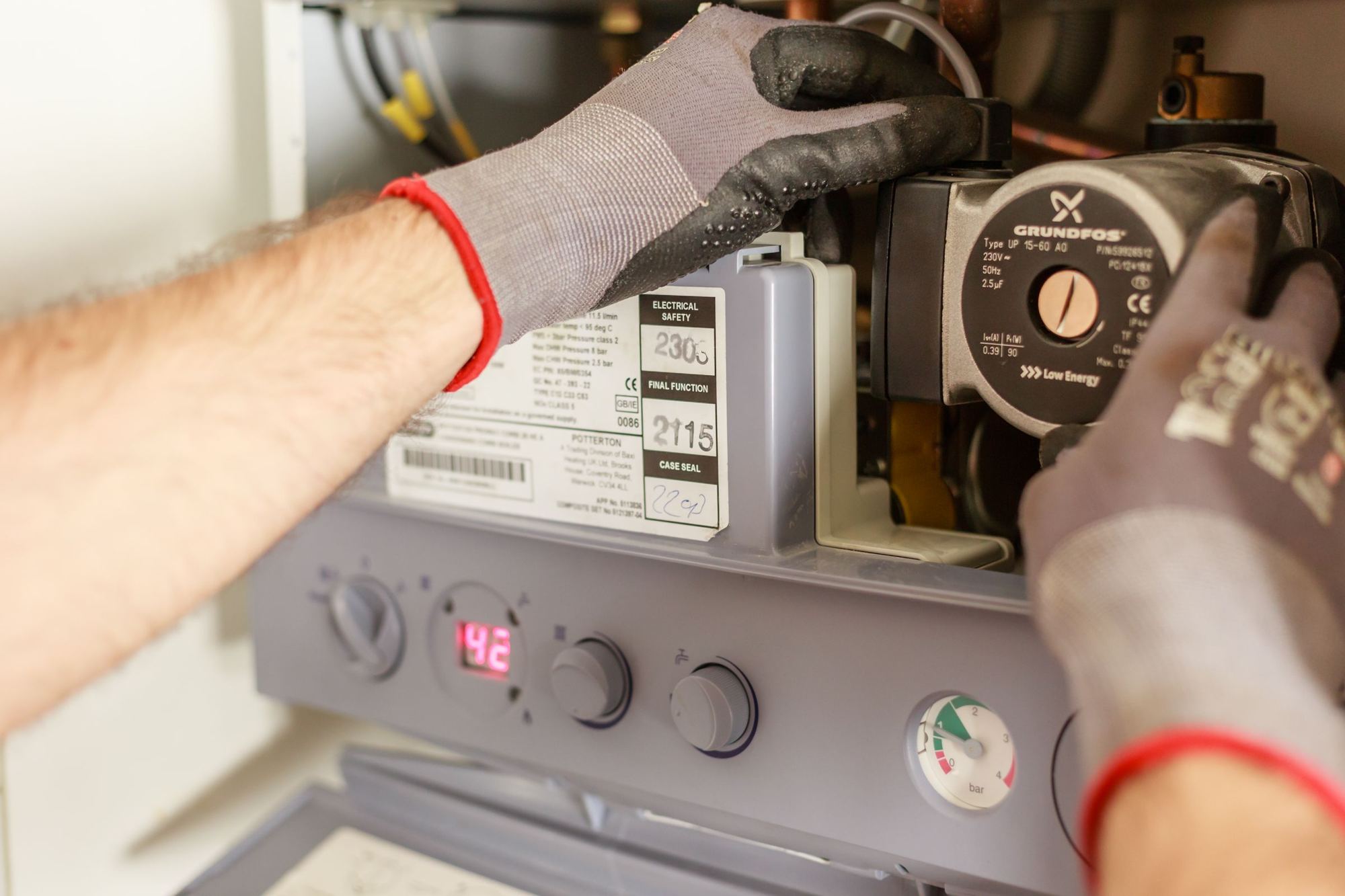 Gloved hands servicing the pump and controls of an open gas boiler